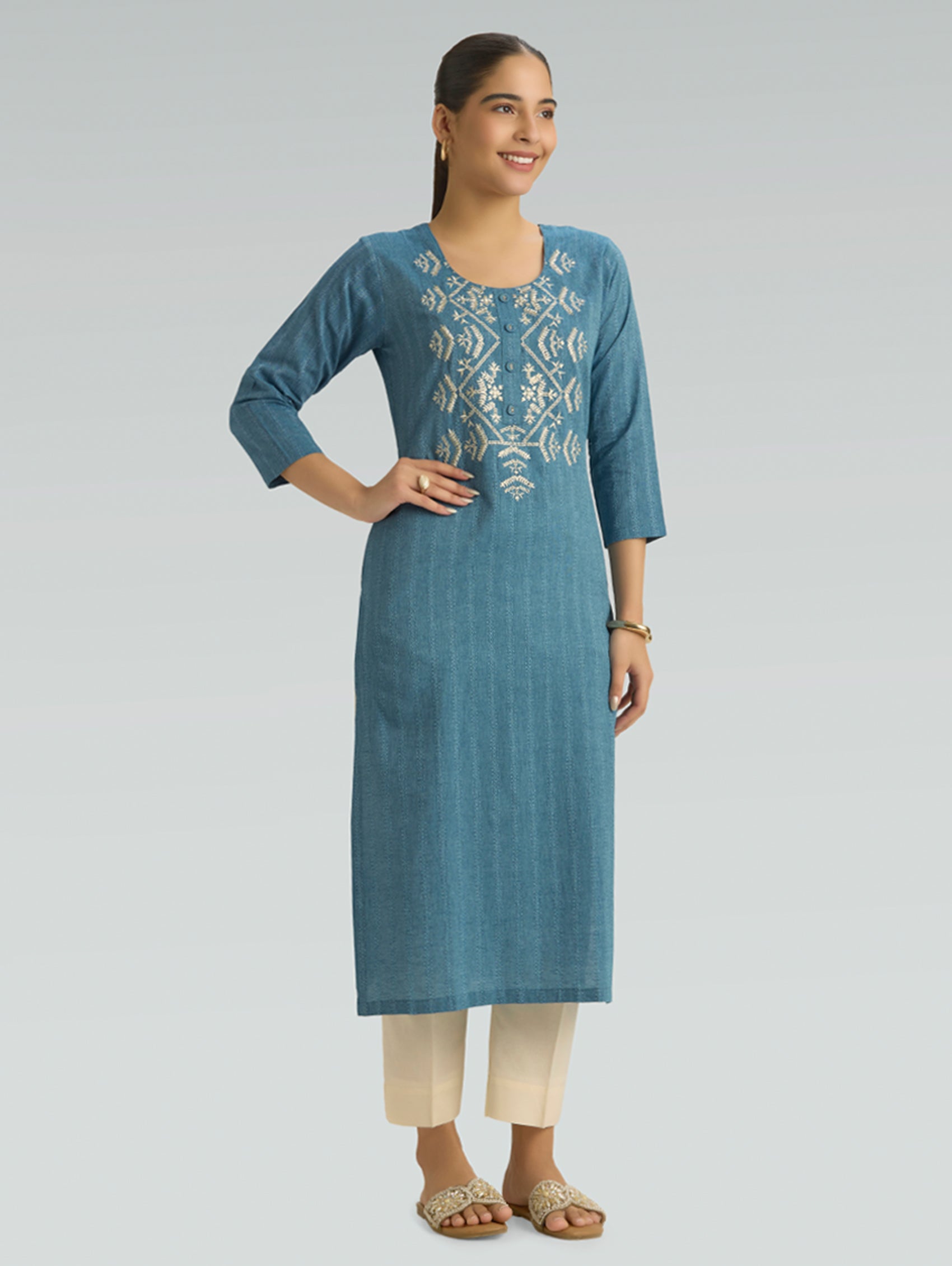 Woman wearing a blue embroidered kurta with beige pants on a gray background