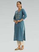 Woman wearing a blue embroidered kurta with beige pants on a gray background