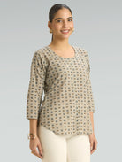 Woman wearing a patterned beige top against a gray background