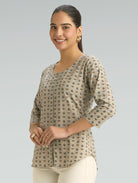 Woman wearing a patterned beige top against a gray background