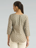 Woman wearing a patterned beige top on a plain background