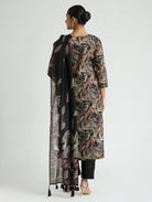 Woman wearing a long, patterned dress with a black scarf over her shoulder on a white background