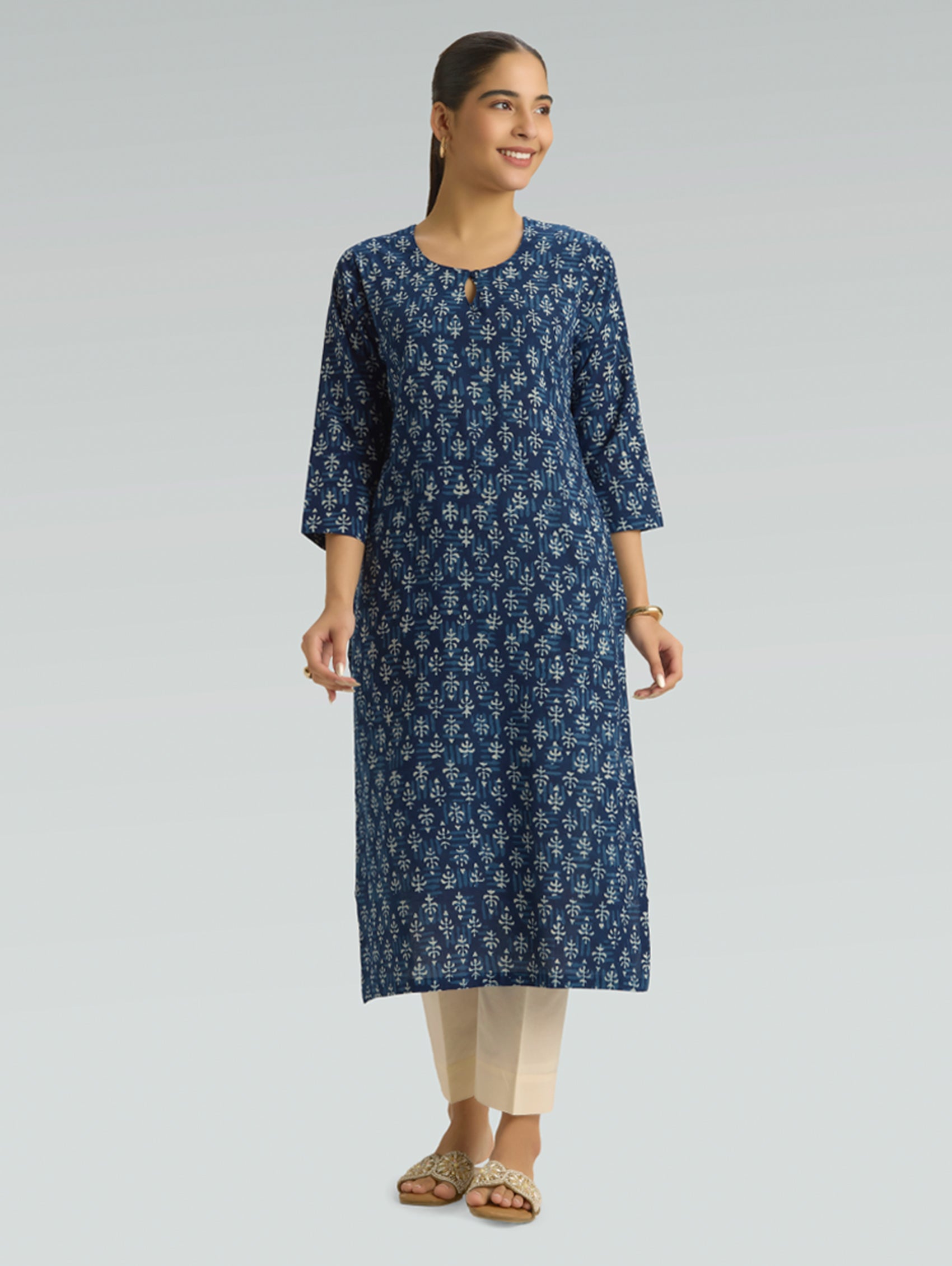 Woman wearing a blue floral kurta with beige pants on a gray background