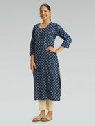 Woman wearing a navy blue patterned kurta with beige pants on a gray background