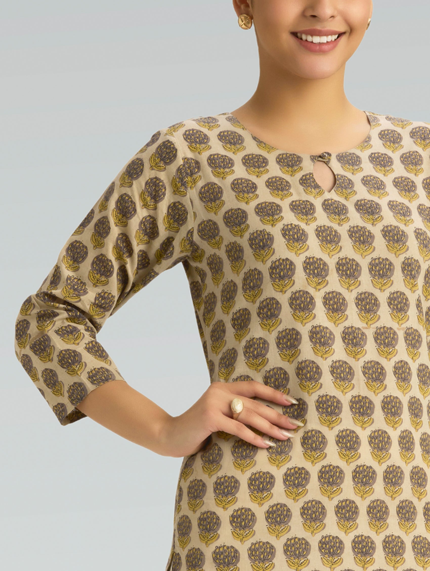 Woman wearing a patterned beige and brown dress against a gray background