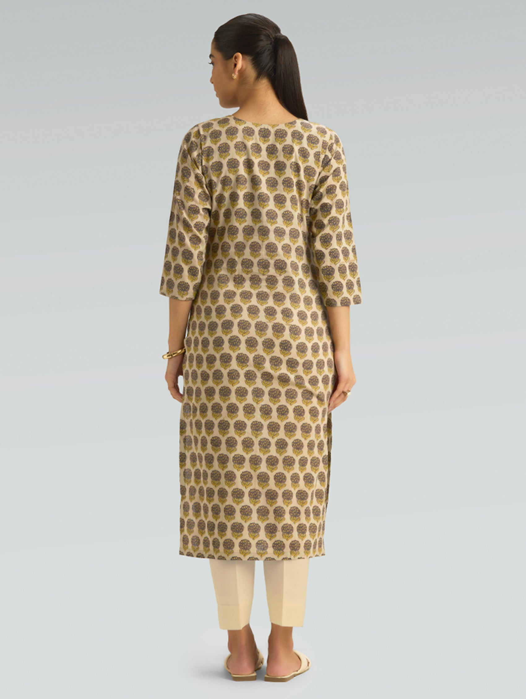 Woman wearing a patterned kurta with beige pants on a gray background